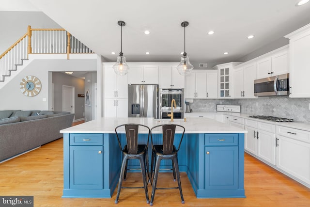 kitchen featuring white cabinets, blue cabinets, a kitchen island with sink, stainless steel appliances, and light wood-type flooring