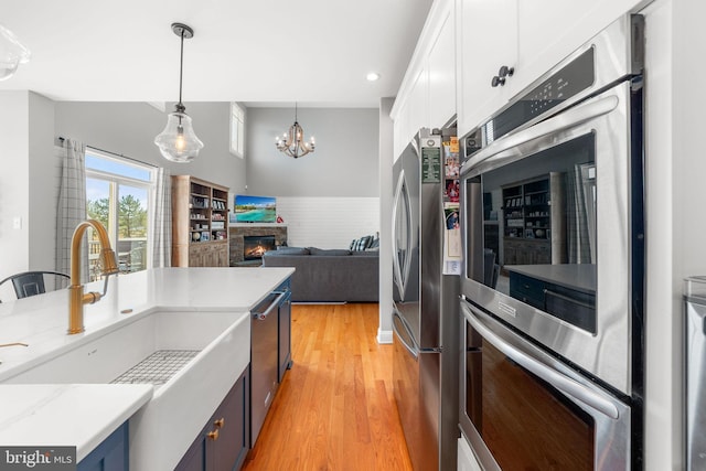 kitchen with pendant lighting, light wood-style floors, freestanding refrigerator, a glass covered fireplace, and white cabinets