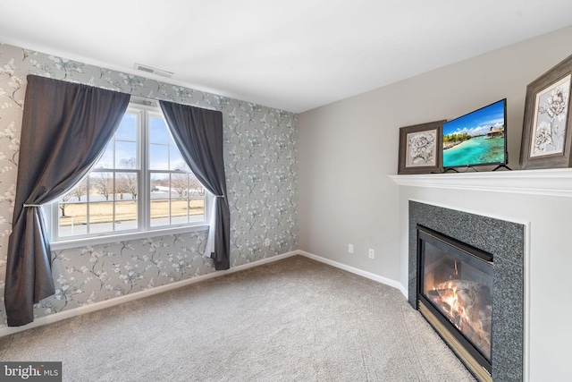 unfurnished living room featuring wallpapered walls, visible vents, baseboards, a glass covered fireplace, and carpet