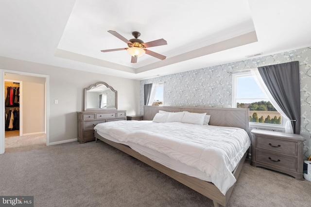 bedroom featuring light carpet, baseboards, a raised ceiling, ceiling fan, and a spacious closet