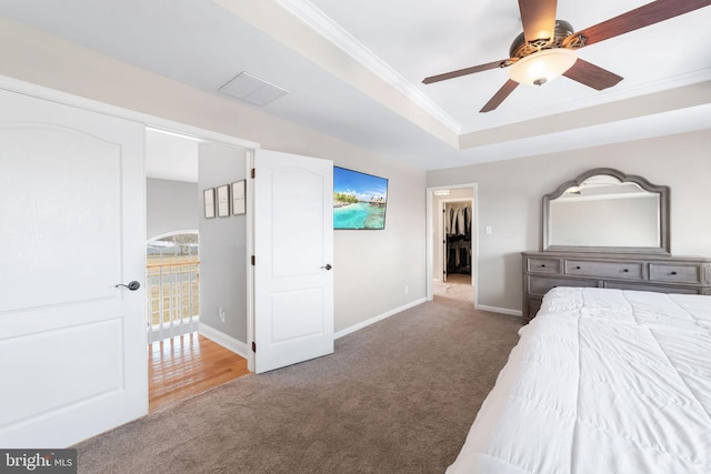 unfurnished bedroom featuring baseboards, a spacious closet, a tray ceiling, carpet, and crown molding