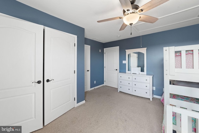 unfurnished bedroom featuring light carpet, attic access, baseboards, ceiling fan, and a closet