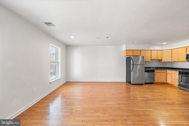 kitchen with stainless steel appliances, dark countertops, light brown cabinets, and light wood-style flooring