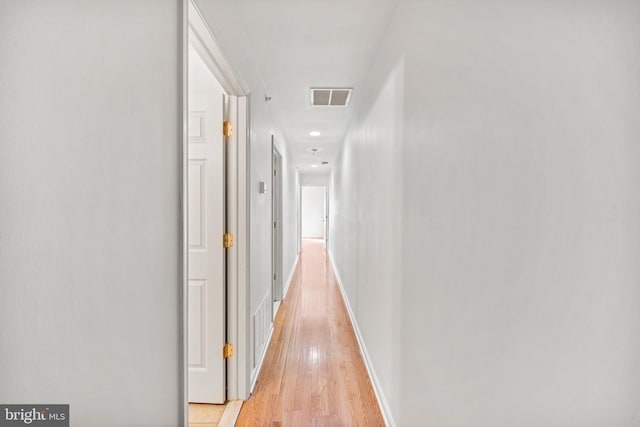 corridor featuring light wood finished floors, baseboards, and visible vents