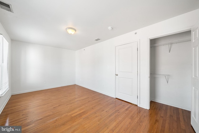 unfurnished bedroom featuring a closet, visible vents, baseboards, and wood finished floors