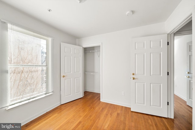 unfurnished bedroom with light wood-type flooring, a closet, and baseboards