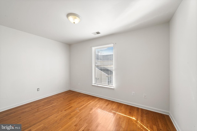 spare room featuring wood finished floors, visible vents, and baseboards