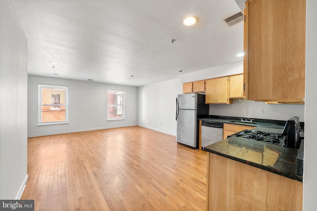 kitchen featuring baseboards, dark stone counters, light wood-style flooring, stainless steel appliances, and a sink