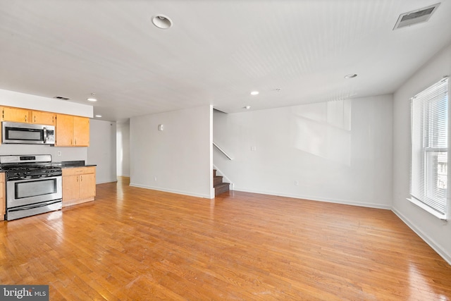 kitchen featuring stainless steel appliances, dark countertops, visible vents, light wood-style flooring, and open floor plan