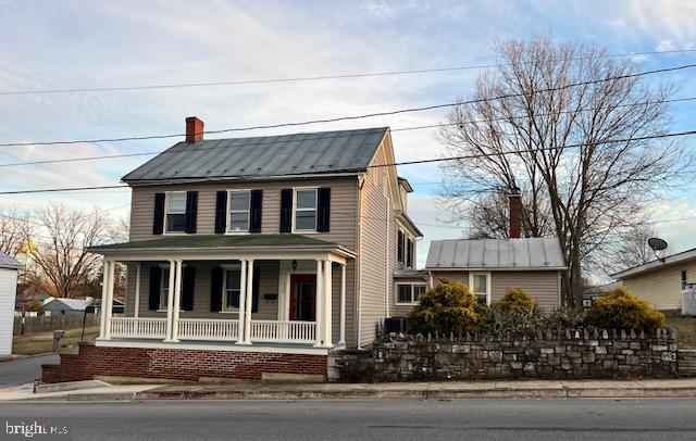 view of front of property featuring covered porch, metal roof, a chimney, and a standing seam roof