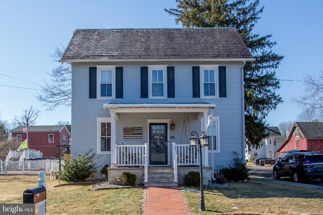 view of front of property featuring covered porch, fence, and a front lawn