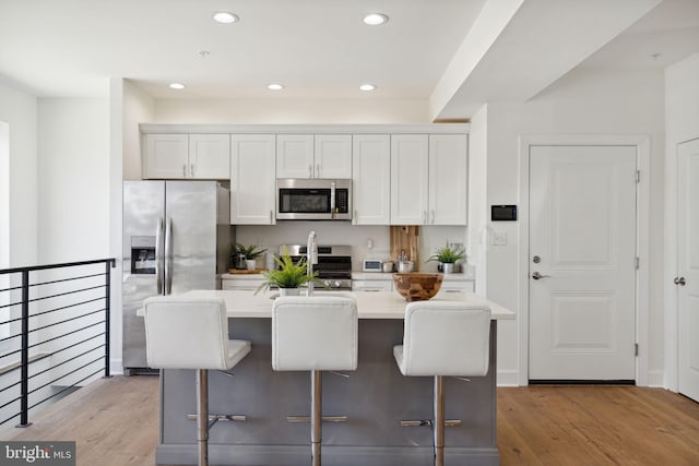 kitchen with a breakfast bar, stainless steel appliances, light countertops, white cabinetry, and an island with sink