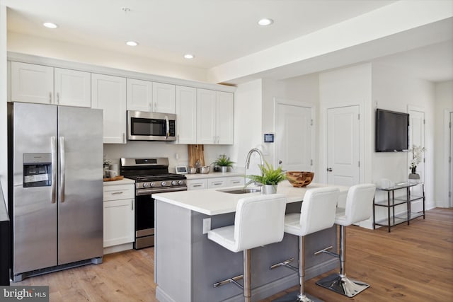 kitchen with appliances with stainless steel finishes, a sink, a center island with sink, and white cabinetry