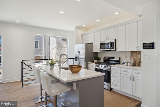 kitchen with light countertops, appliances with stainless steel finishes, a kitchen island with sink, and white cabinets