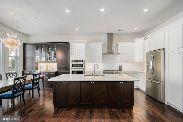 kitchen with glass insert cabinets, appliances with stainless steel finishes, light countertops, wall chimney range hood, and a sink