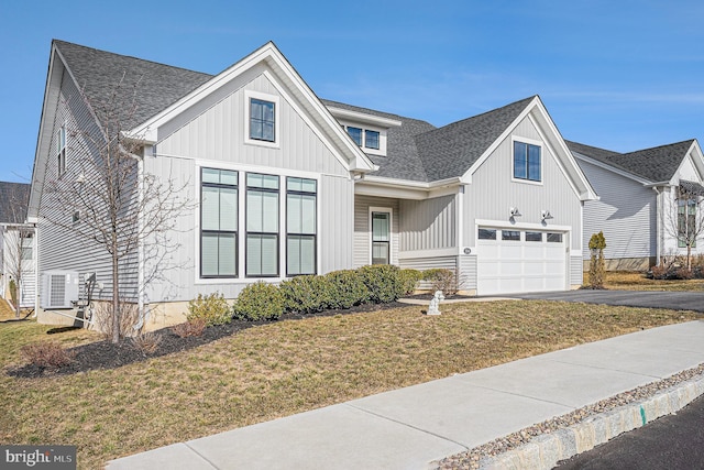 modern inspired farmhouse featuring a front lawn, a shingled roof, an attached garage, and aphalt driveway