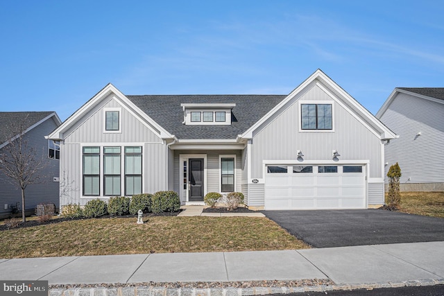 view of front of house featuring an attached garage, a shingled roof, aphalt driveway, and a front yard