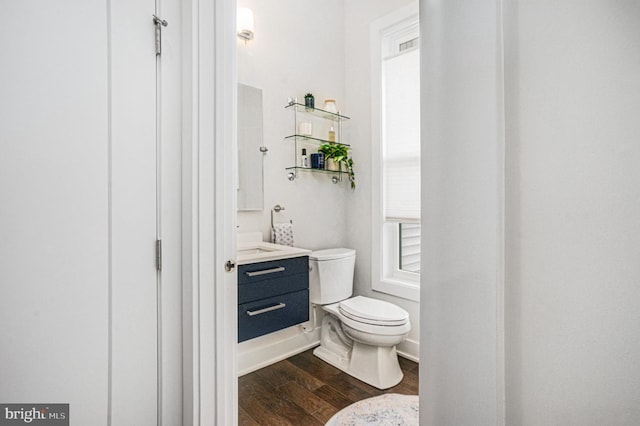 half bathroom with baseboards, vanity, toilet, and wood finished floors