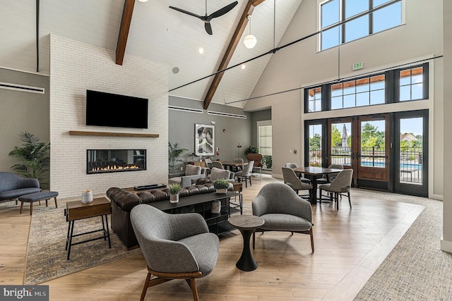 living room with beam ceiling, french doors, light wood finished floors, a glass covered fireplace, and high vaulted ceiling