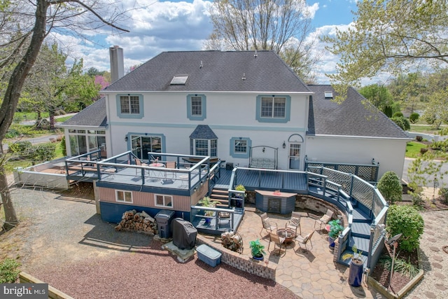 back of property with roof with shingles, a chimney, stucco siding, and a deck