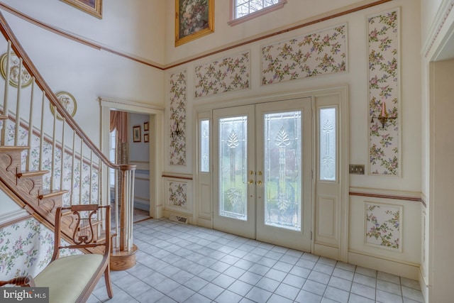 entrance foyer with french doors, light tile patterned flooring, a high ceiling, stairs, and a decorative wall