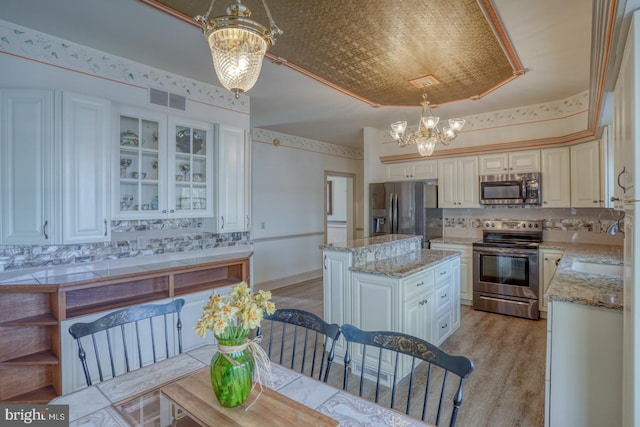 kitchen with stainless steel appliances, visible vents, a kitchen island, tasteful backsplash, and a notable chandelier