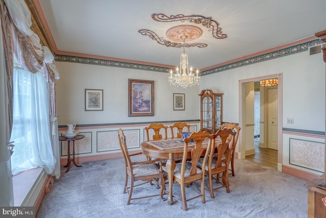 carpeted dining space with plenty of natural light, visible vents, a wainscoted wall, and an inviting chandelier