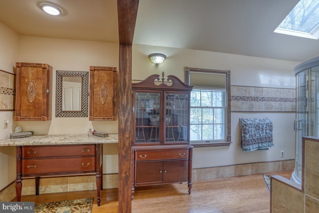 interior space featuring a shower with door, vanity, wood finished floors, and a skylight