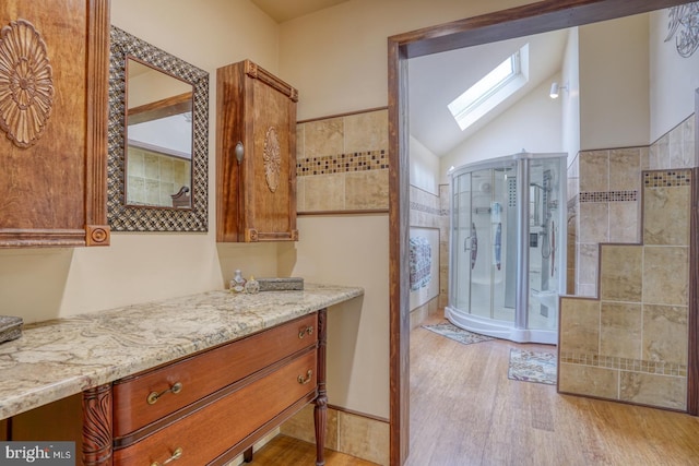 full bath featuring wood finished floors, lofted ceiling with skylight, vanity, and a stall shower