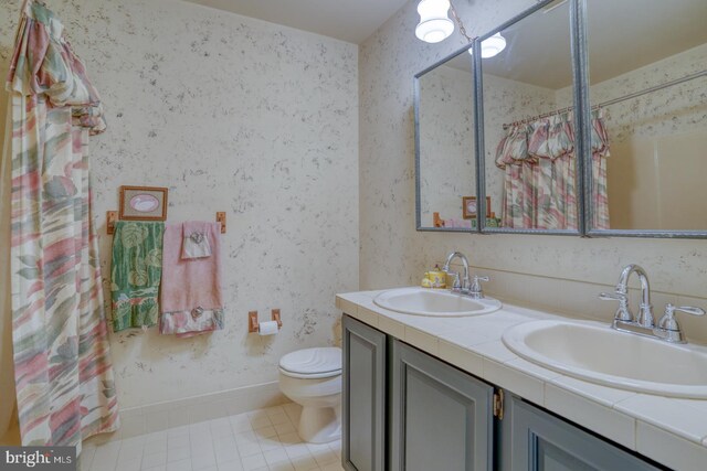 full bath featuring toilet, a sink, wallpapered walls, and double vanity