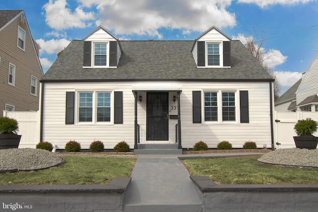 new england style home featuring roof with shingles, a front yard, and fence