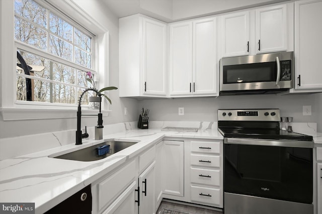 kitchen with white cabinetry, appliances with stainless steel finishes, light stone counters, and a sink