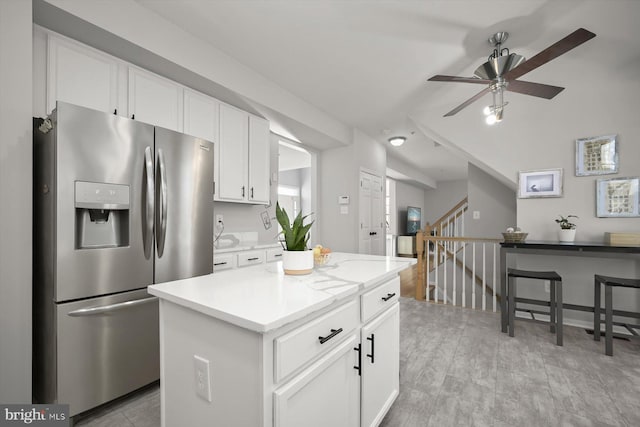 kitchen with stainless steel refrigerator with ice dispenser, light countertops, white cabinetry, a kitchen island, and ceiling fan