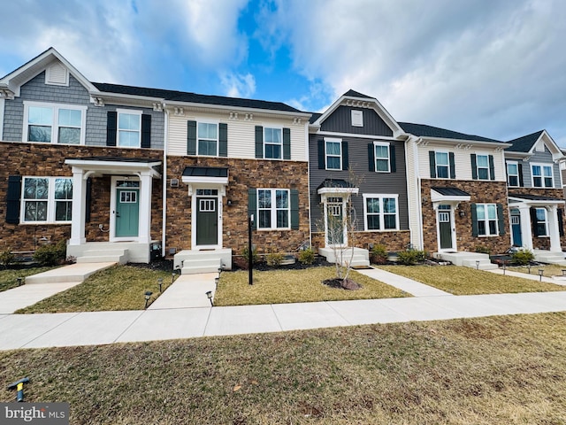 townhome / multi-family property with stone siding and a front yard