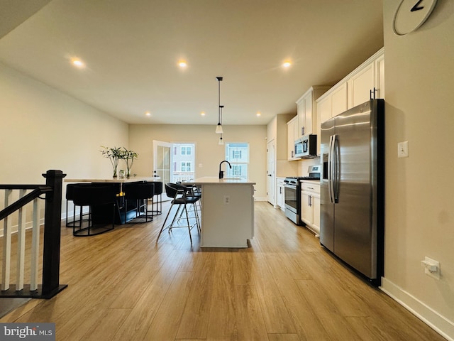 kitchen featuring light wood finished floors, white cabinetry, a kitchen island with sink, and appliances with stainless steel finishes