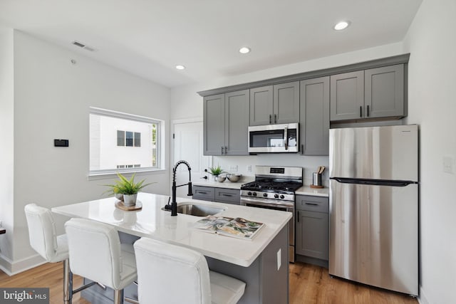 kitchen featuring stainless steel appliances, gray cabinets, light countertops, a sink, and an island with sink