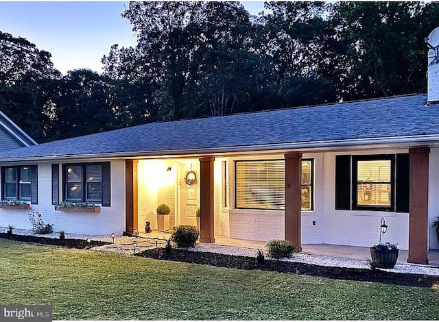 single story home with brick siding, covered porch, a shingled roof, and a front lawn