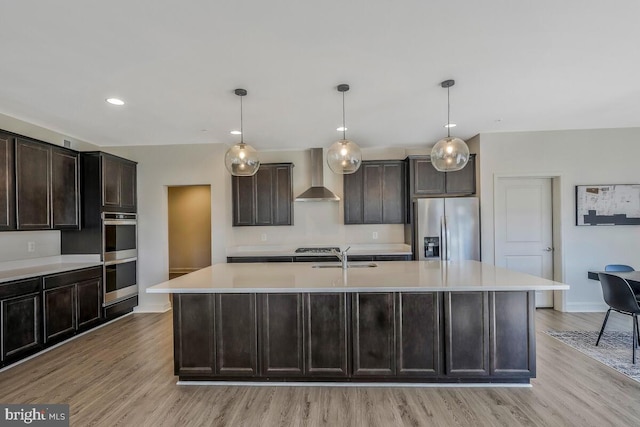 kitchen with stainless steel appliances, wall chimney exhaust hood, light countertops, and a center island with sink