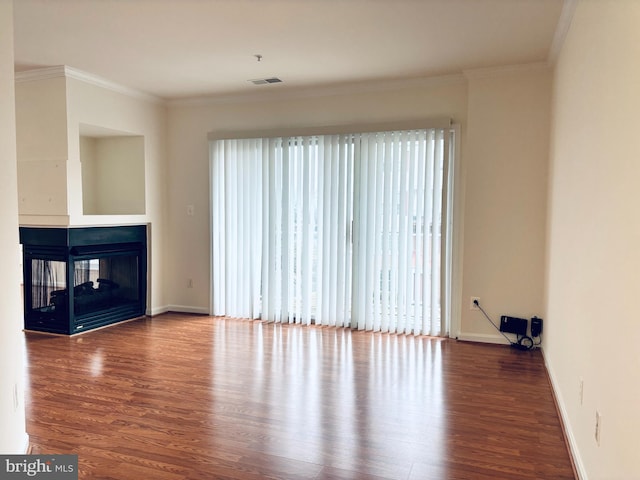 unfurnished living room with wood finished floors, a multi sided fireplace, visible vents, and crown molding