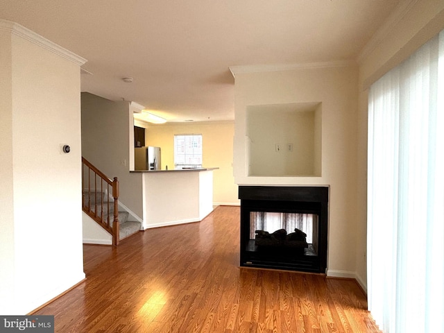 unfurnished living room with ornamental molding, stairway, a multi sided fireplace, and wood finished floors