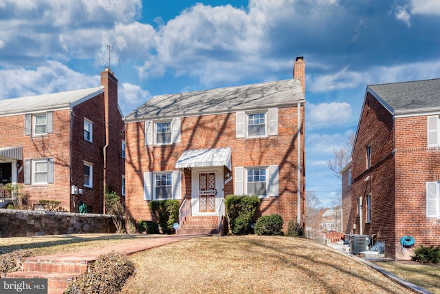 view of front of home featuring central AC, brick siding, a chimney, and a front lawn