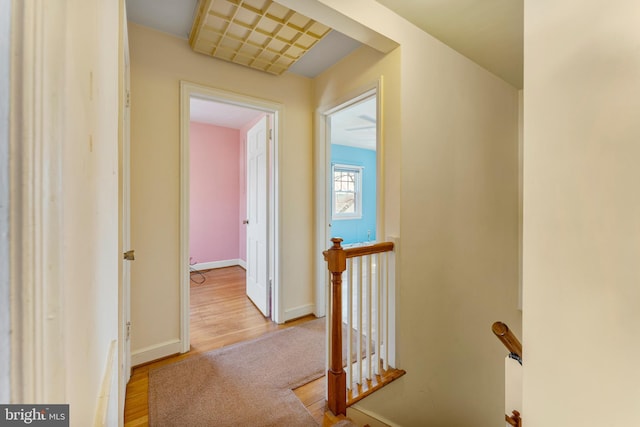 hall with light wood-style floors, baseboards, and an upstairs landing