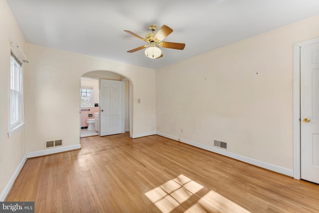 empty room featuring arched walkways, light wood-style flooring, visible vents, and baseboards