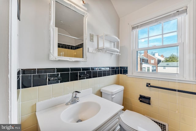 bathroom with toilet, a sink, tile walls, vaulted ceiling, and wainscoting