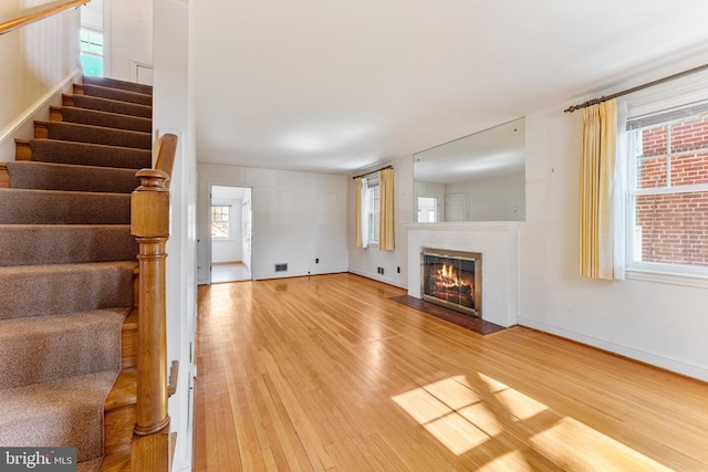 unfurnished living room featuring a fireplace with flush hearth, stairs, baseboards, and wood finished floors