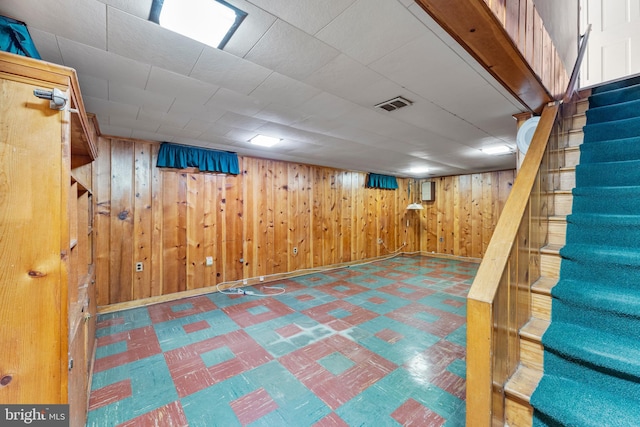 finished below grade area featuring stairway, visible vents, wooden walls, and tile patterned floors