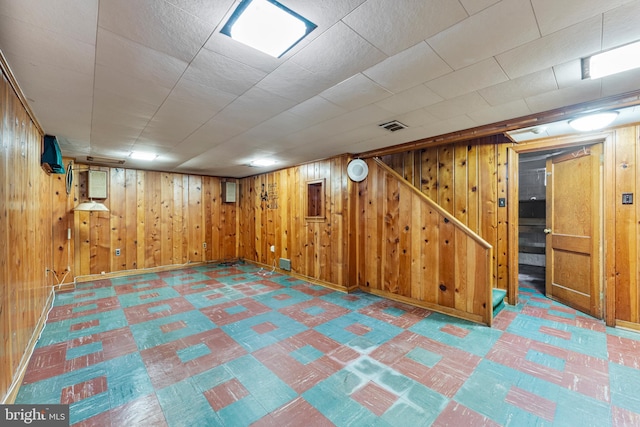 finished below grade area with tile patterned floors, visible vents, wooden walls, baseboards, and stairs