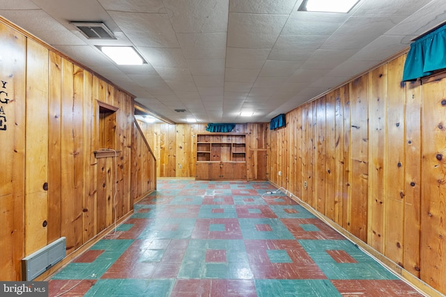 finished basement with wood walls, visible vents, and tile patterned floors