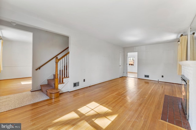 unfurnished living room with stairs, visible vents, a fireplace, and wood finished floors