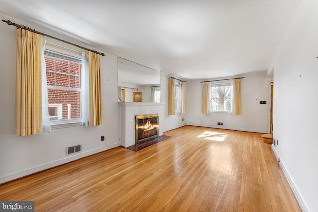 unfurnished living room with light wood-type flooring, a fireplace with flush hearth, visible vents, and baseboards